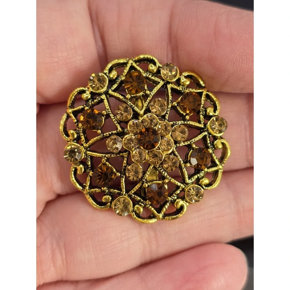 gold-tone brooch with a filigree design and amber/brown rhinestones